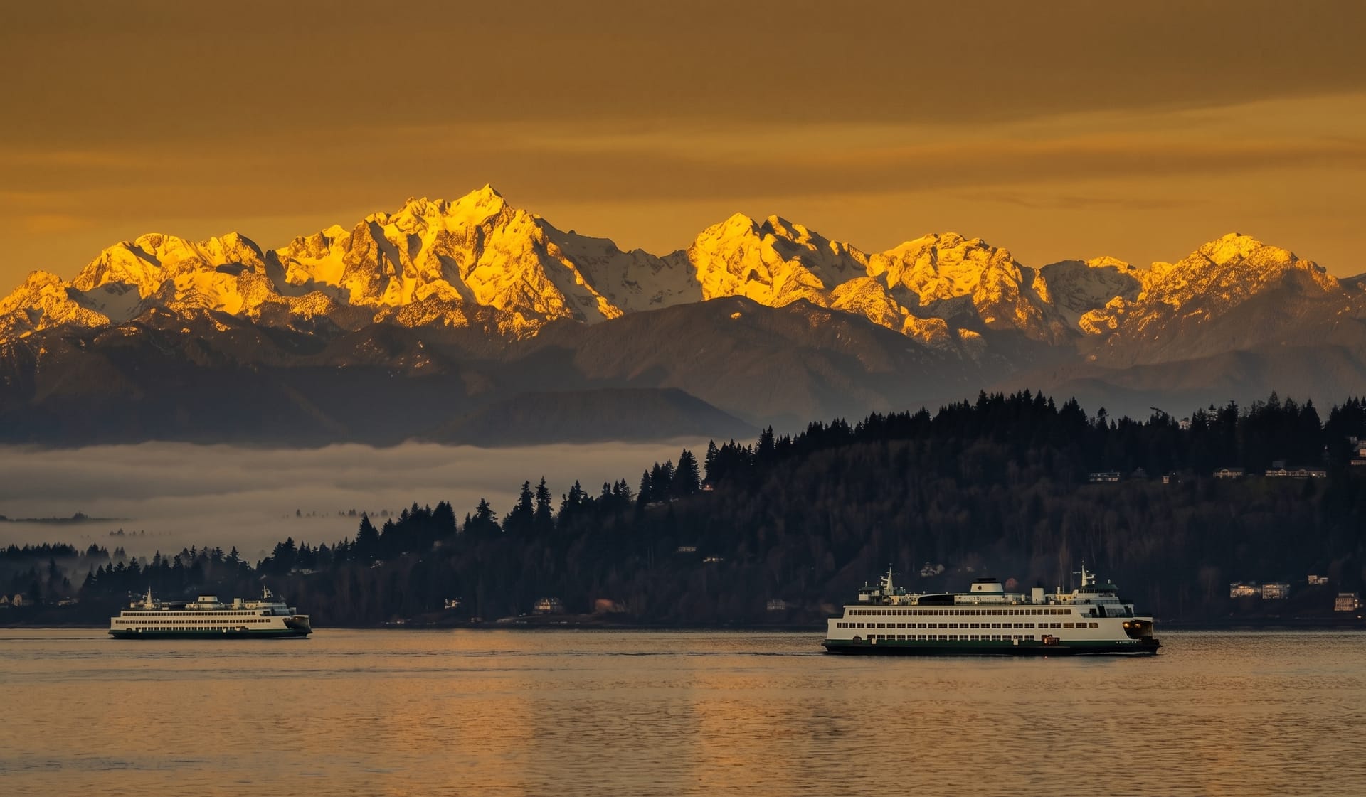 The Olympic Mountains lit gold at sunset across Puget Sound, with two Washington State ferries passing in the channel below.